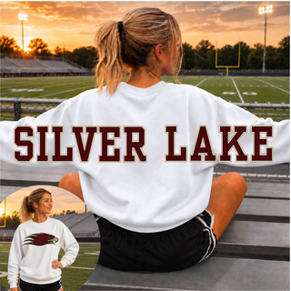 Woman wearing an oversized white Silver Lake Eagles crewneck sweatshirt at a football field, with the SILVER LAKE wordmark in maroon and gold across the back