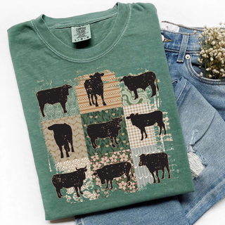 Folded light green Comfort Colors t shirt with nine black cattle silhouettes on vintage patchwork quilt squares with floral gingham and boho patterns next to blue jeans