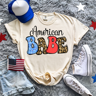 Ivory Comfort Colors tee flat lay with american babe patriotic graphic, american flag and sneakers
