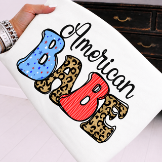 White tee held up showing american babe patriotic stars leopard and red wave lettering graphic
