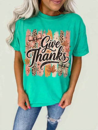 Woman in the Pink Friday Give Thanks Leopard Bow Island Green Top with script lettering, bows, and fall leaves