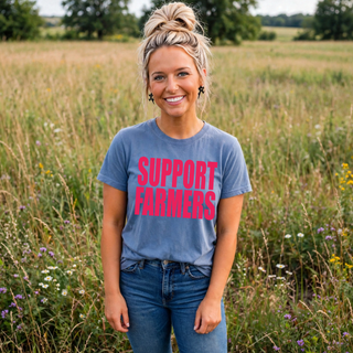 Woman wearing blue jean support farmers top with bold pink block lettering in a field