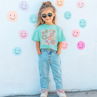 Young girl wearing Retro Checkered Smiley Flower Graphic Tee in chalky mint with pastel daisy and smiley face checker design
