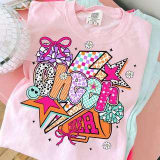 Light pink graphic top with colorful retro cheer design featuring pom poms bows stars lightning bolt and mixed print letters folded on pink surface with disco ball