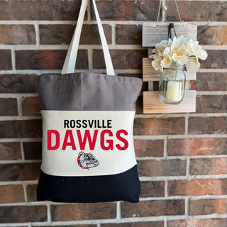 Rossville Bulldawgs three-tone canvas tote bag in grey, natural, and black with Rossville Dawgs text and bulldog mascot, hanging on brick wall
