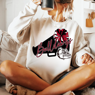 Woman seated on couch in heather dust crewneck with Bulldawgs megaphone pom poms and bulldog mascot design, holding dark mug
