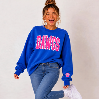 Model wearing a royal blue crewneck with pink leopard-style DAWGS lettering and a matching paw print sleeve accent