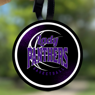 Round black bag tag with a white border and a purple Lady Panthers Basketball design hanging from a strap outdoors