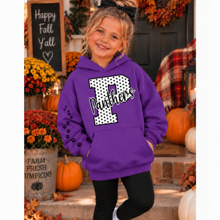 Girl in a purple hoodie with a white polka dot letter P outlined in black, black Panthers script, and black paw prints down the sleeve, standing on a fall porch with pumpkins