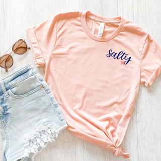 Heather peach Bella Canvas tee with Salty script and starfish pocket design styled with denim shorts and sunglasses