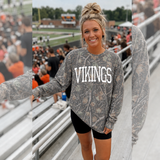Woman wearing Seaman Vikings camo long sleeve in deadwood tree camo at a football stadium in a navy hat and black shorts
