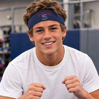 Smiling wrestler wearing a navy PosiCharge headband with red arched Wrestling above a red and navy S logo