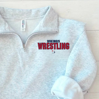 Close-up of an ash grey cadet quarter-zip with Vikings above red Wrestling lettering and an S logo beneath, resting on a light wood surface