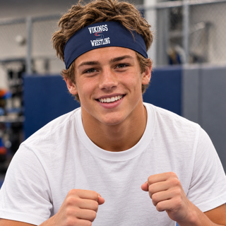 Smiling wrestler wearing a navy PosiCharge headband with white Vikings stacked above a red and navy S logo and Wrestling