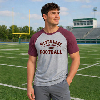 Male model wearing a grey and maroon Silver Lake Eagles Football Classic men’s raglan top on a football field