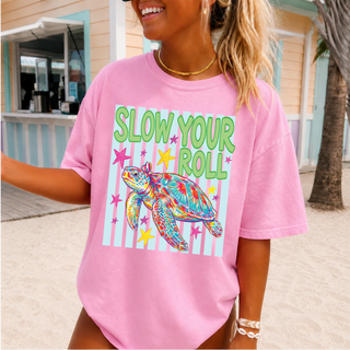 blossom Comfort Colors tee with slow your roll sea turtle striped graphic and stars, worn by a smiling woman at the beach
