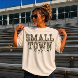 Ivory adult Small Town Big Pride Camo graphic top model holding shirt at bleachers