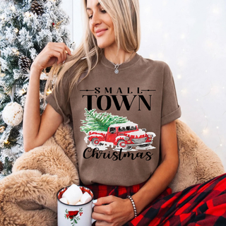 Model wearing a brown Comfort Colors tee with Small Town lettering, a red vintage truck carrying a Christmas tree, and Christmas script