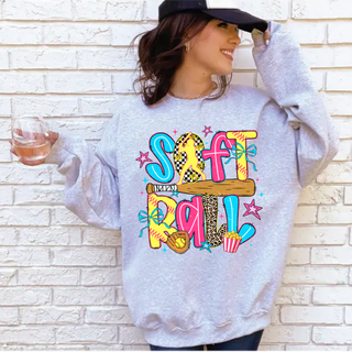 Woman wearing Gildan ash grey crewneck sweatshirt with colorful pink yellow and blue doodle softball graphic featuring player bat glove bows leopard print and checkered letters