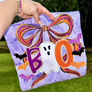 purple tie dye adult top with boo ghost bow bats halloween design, held outdoors on grass
