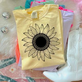 Comfort Colors banana short sleeve tee with large black and cream detailed sunflower graphic laid flat with white cowboy boots