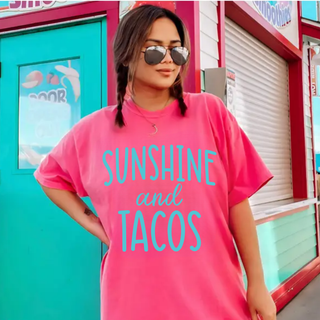 Woman wearing a crunchberry tee with SUNSHINE and TACOS turquoise graphic printed on the front

