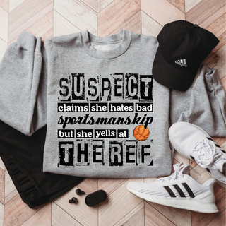 Gray crewneck sweatshirt flat lay with black and white distressed lettering reading Suspect claims she hates bad sportsmanship but she yells at the ref, with an orange basketball graphic