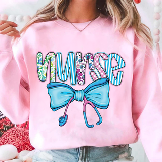 Model wearing light pink crewneck with nurse patterned letters blue bow and stethoscope design
