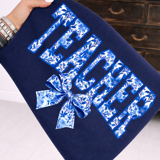 Hand holding navy top with TEACHER blue chinoiserie floral varsity letters and coquette bow, adult unisex