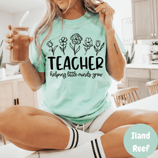 Woman wearing island reef Comfort Colors tee with TEACHER helping little minds grow floral line art design
