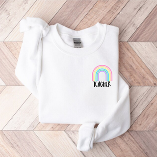 White Gildan crewneck with pastel rainbow and Teacher text left chest pocket design flat lay