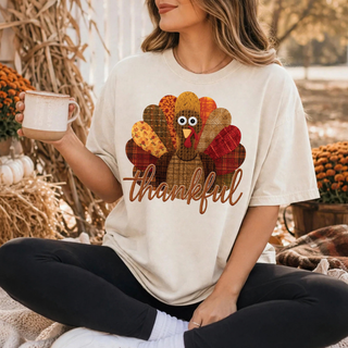 Thankful patchwork turkey design with googly eyes on a sand Comfort Colors tee, with "thankful" in brown script lettering below