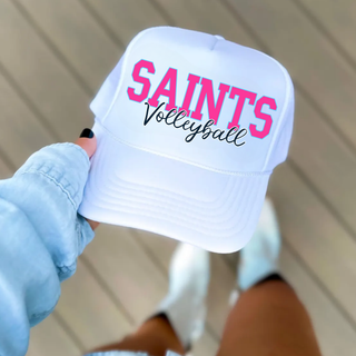 White trucker hat with pink Saints Volleyball script logo held up outdoors