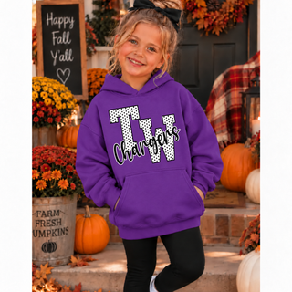 Girl in a purple hoodie with white polka dot TW letters outlined in black and black Chargers script on the front, with plain sleeves, standing on a fall porch with pumpkins