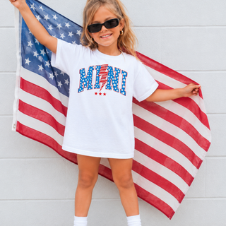 Little girl holding american flag wearing white tee with vintage all american mini arched blue star lightning bolt design
