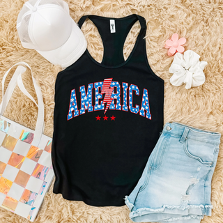 black Next Level racerback tank featuring america stars and stripes lightning bolt graphic, with denim shorts and white hat

