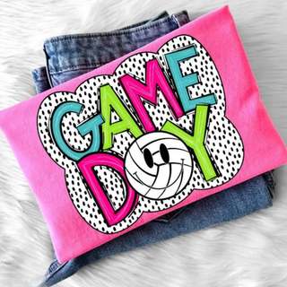 Hot pink tee laid flat with GAME DAY colorful retro polka dot volleyball smiley graphic on the front
