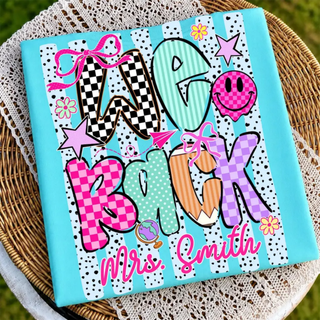 Teal We Back personalized name graphic tee with checkered lettering and smiley face on wicker chair