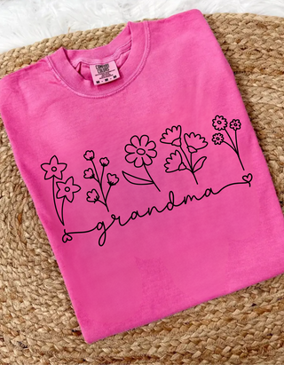 Crunchberry Comfort Colors tee folded on wicker with wildflower line art and grandma script graphic
