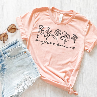 Peach Bella Canvas tee with wildflower line art and grandma script graphic, flat lay with sunglasses
