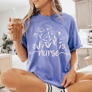 Woman in periwinkle Comfort Colors tee with white wildflower bouquet and nurse script graphic
