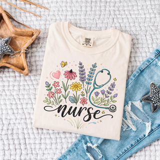 Ivory Comfort Colors tee with wildflower bouquet stethoscope and nurse script graphic design laid flat with denim