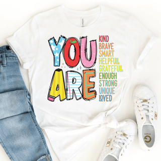 White tee with colorful YOU ARE apple pencil letters and affirmation words, flat lay with jeans and sneakers